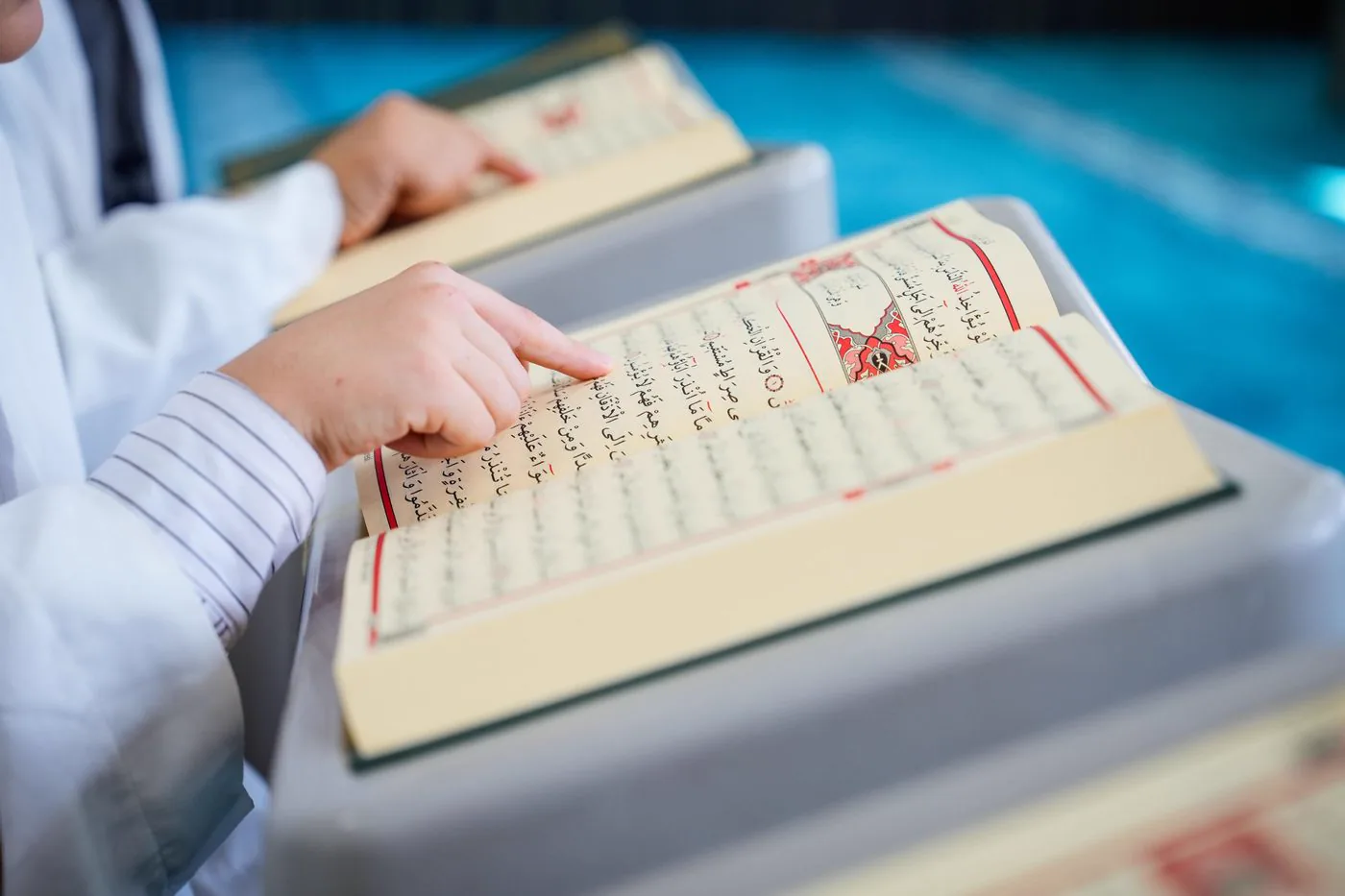 Child's finger following the verses in an open Quran