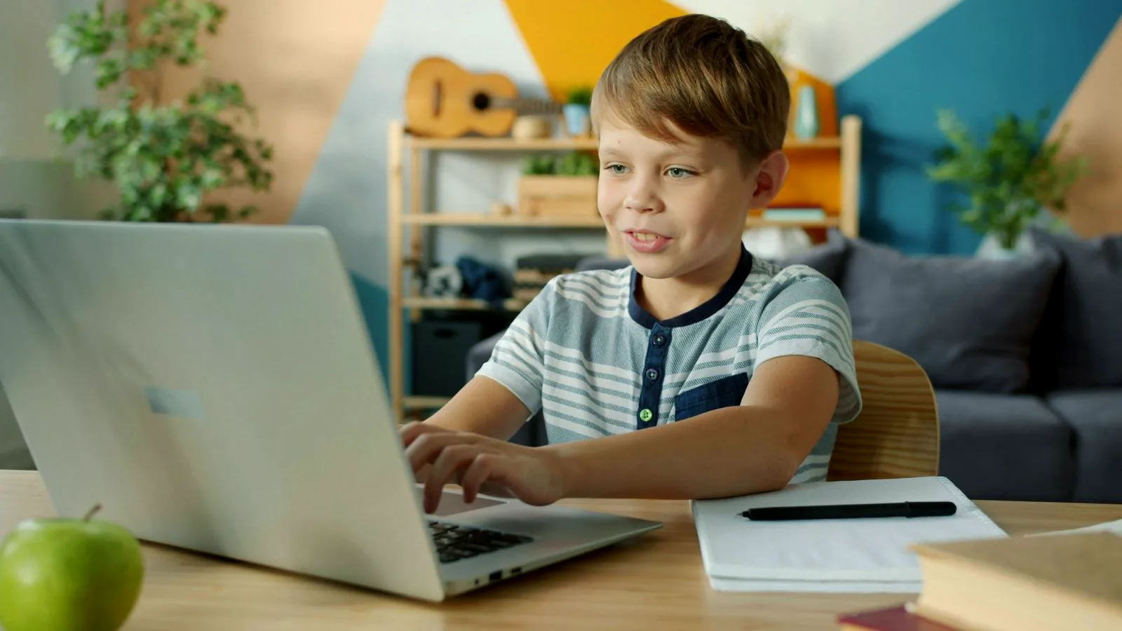 Boy learning online with a laptop and notebook at home